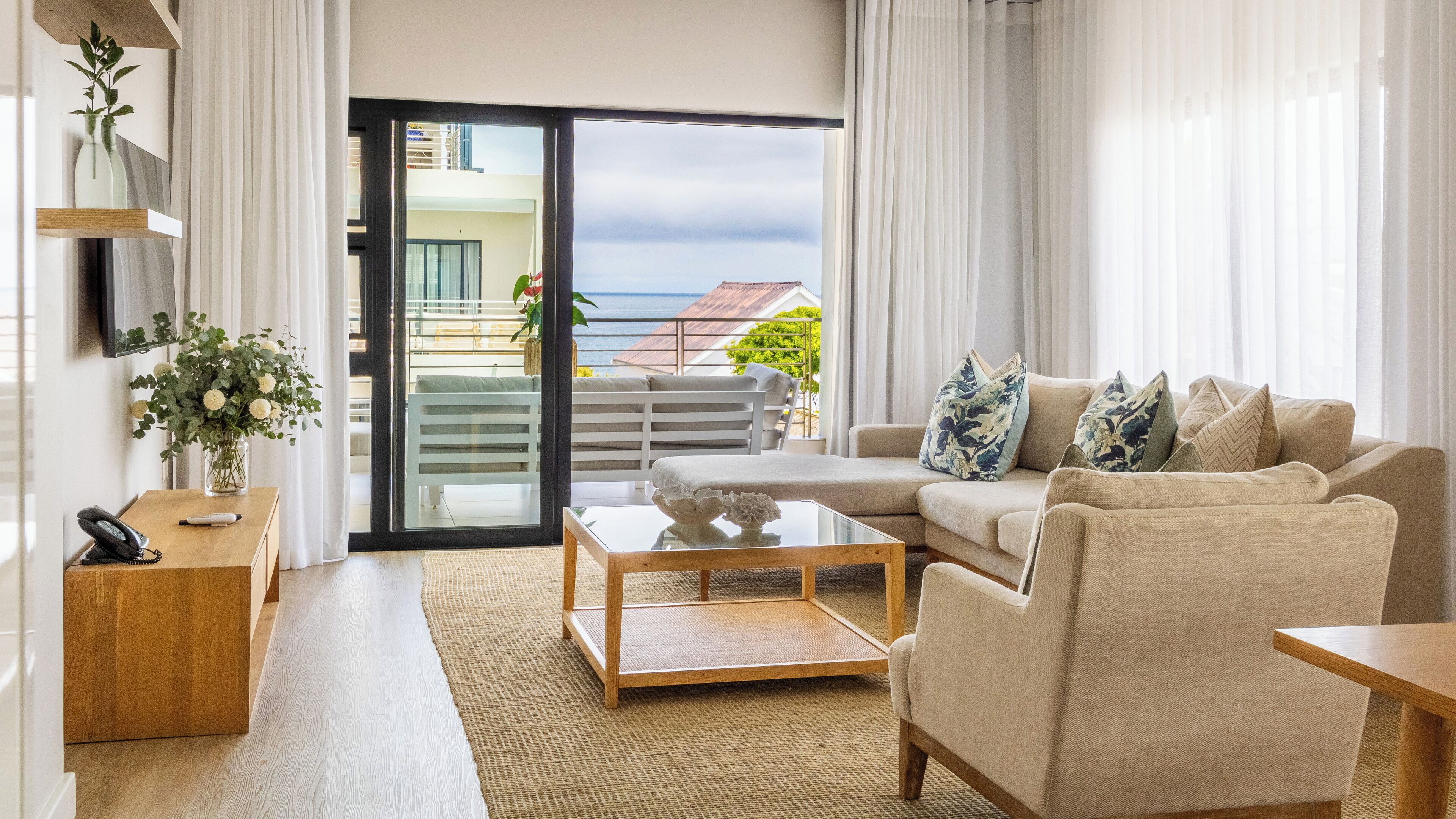 Ein modernes Wohnzimmer mit einer Couch, einem Couchtisch und Meerblick durch eine Glastür.