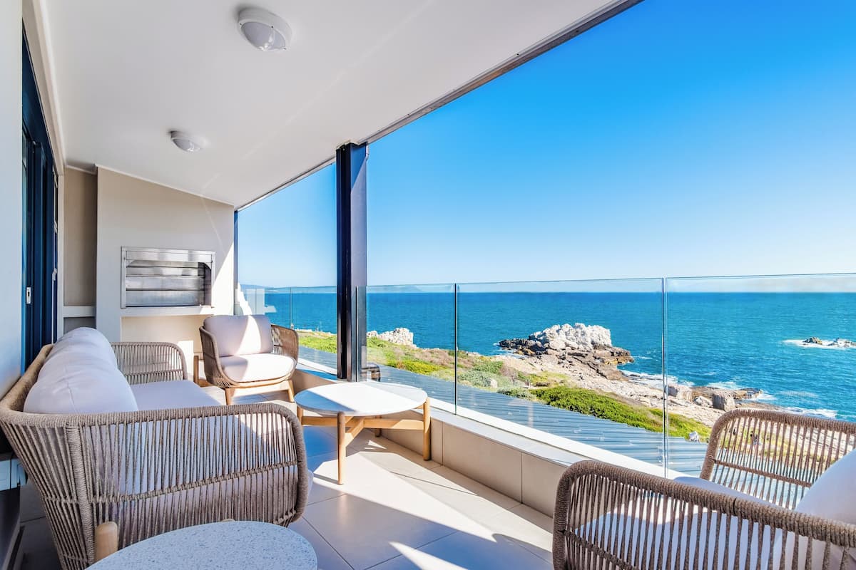 Un balcon agrémenté de meubles en osier, d’une petite table et offrant une vue sur la mer et la côte rocheuse.