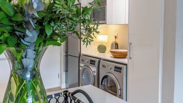 A compact kitchen with a washing machine, a microwave, and a small dining area with a bowl and a lamp.