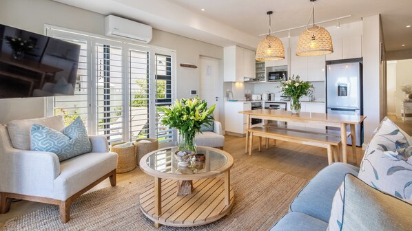 A modern living room with a round coffee table, sofas, a TV, and a kitchen area with a dining table.