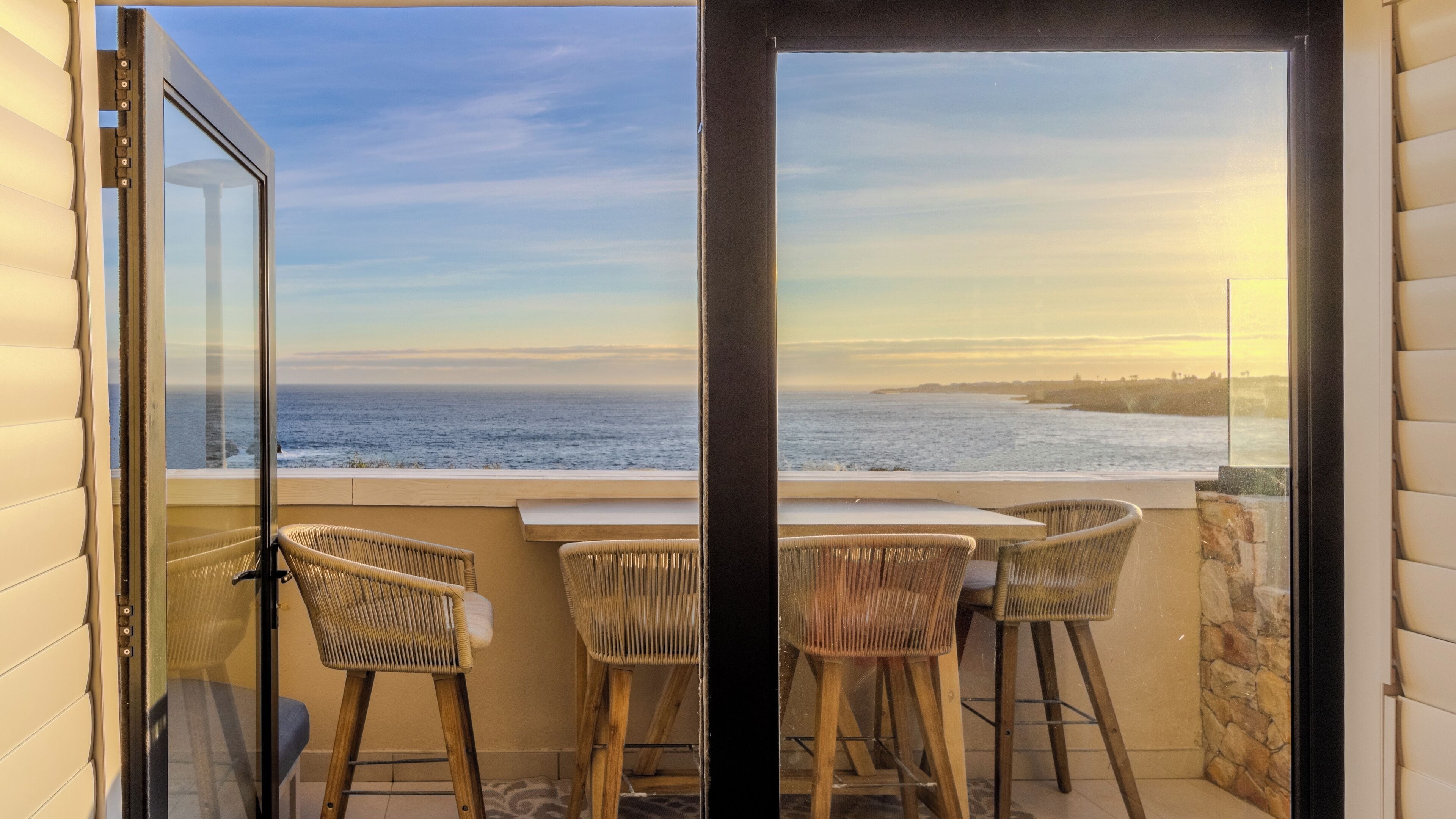 Een balkon met rieten stoelen en uitzicht op de oceaan.