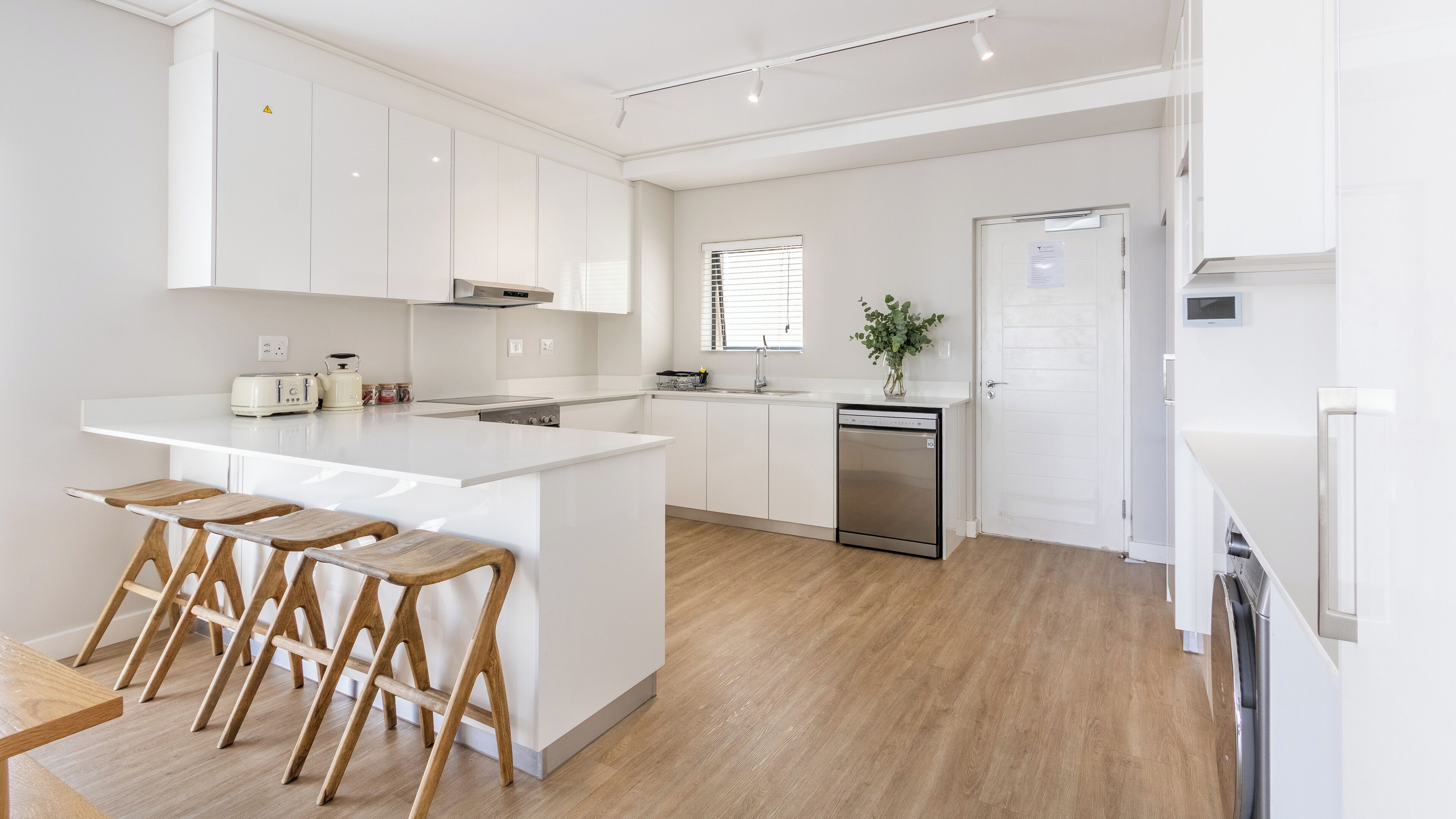 A modern kitchen with white cabinetry, a central island with bar stools, a dishwasher, and a refrigerator.