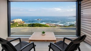 A balcony with a view of the ocean, a small table with a plant, and two chairs.