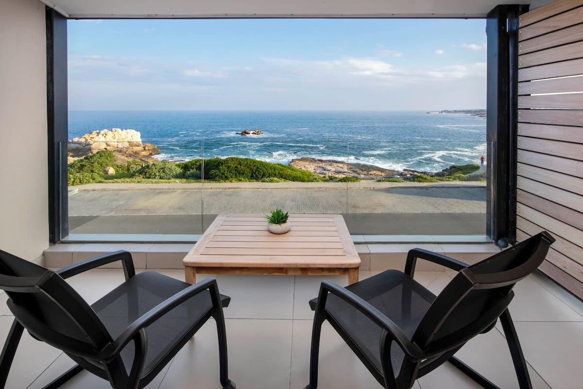 Un balcon avec vue sur l’océan, une petite table avec une plante et deux chaises.