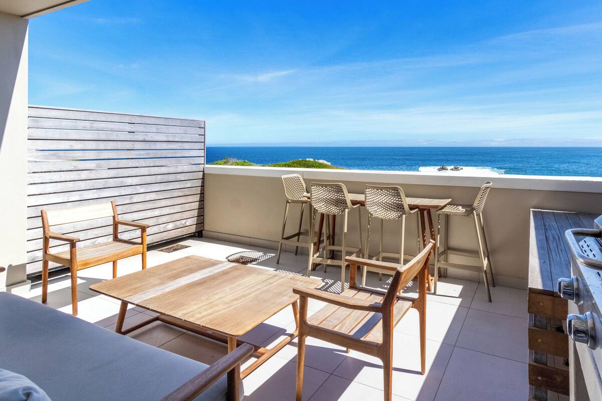 Un balcon avec une table en bois, quatre chaises en osier et un barbecue.