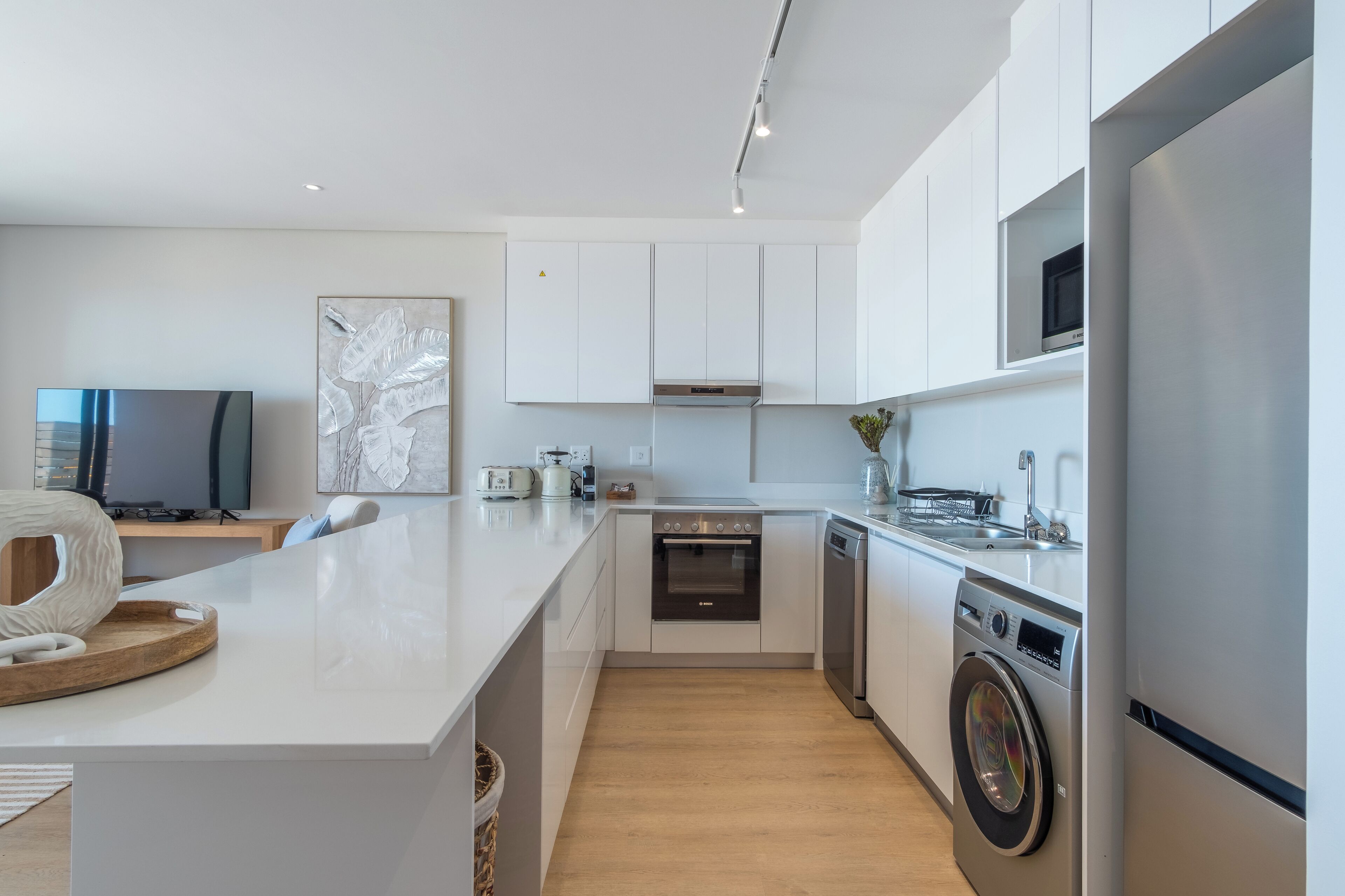 A modern kitchen with white cabinetry, a built-in oven, a dishwasher, and a large island with a microwave and kettle.