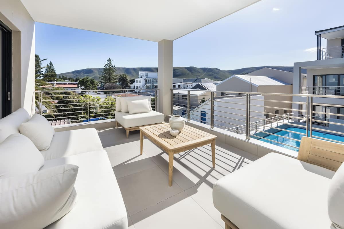 Un balcon avec des canapés blancs, une table en bois et une piscine.