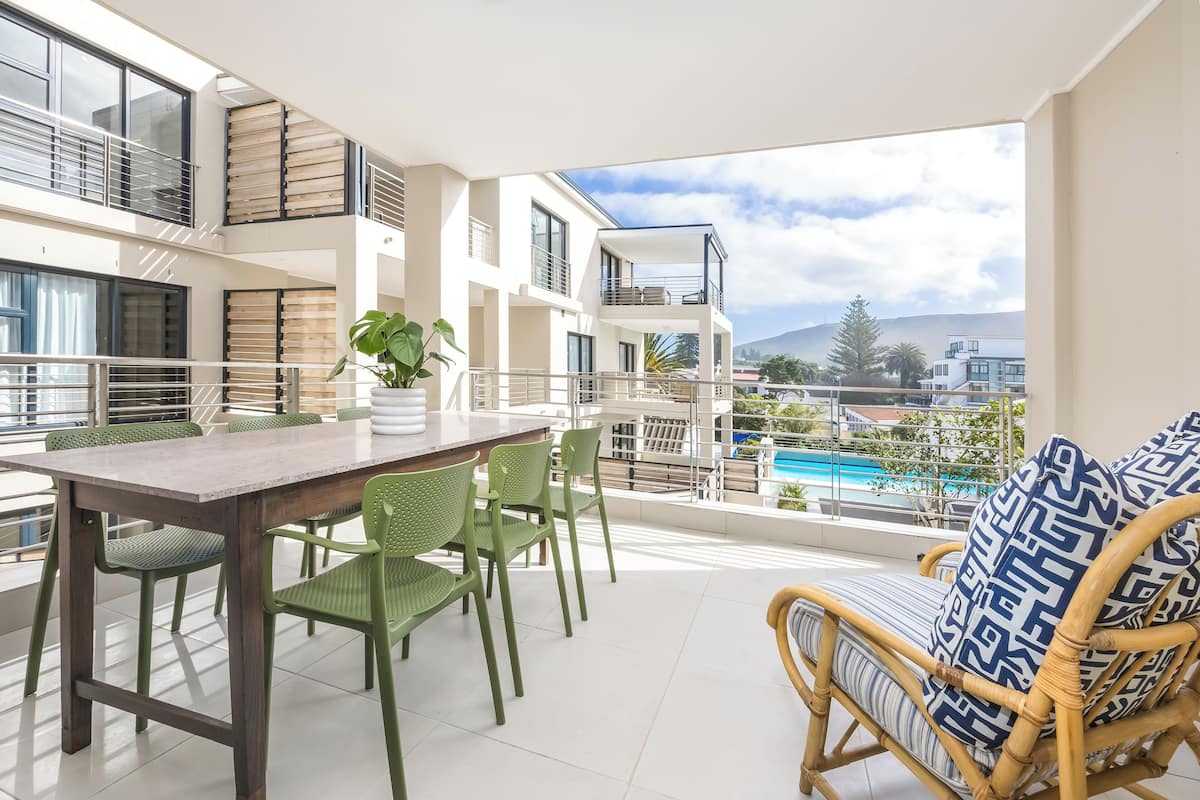 Un balcon avec une table à manger, des chaises et un canapé en osier agrémenté de coussins à motifs.