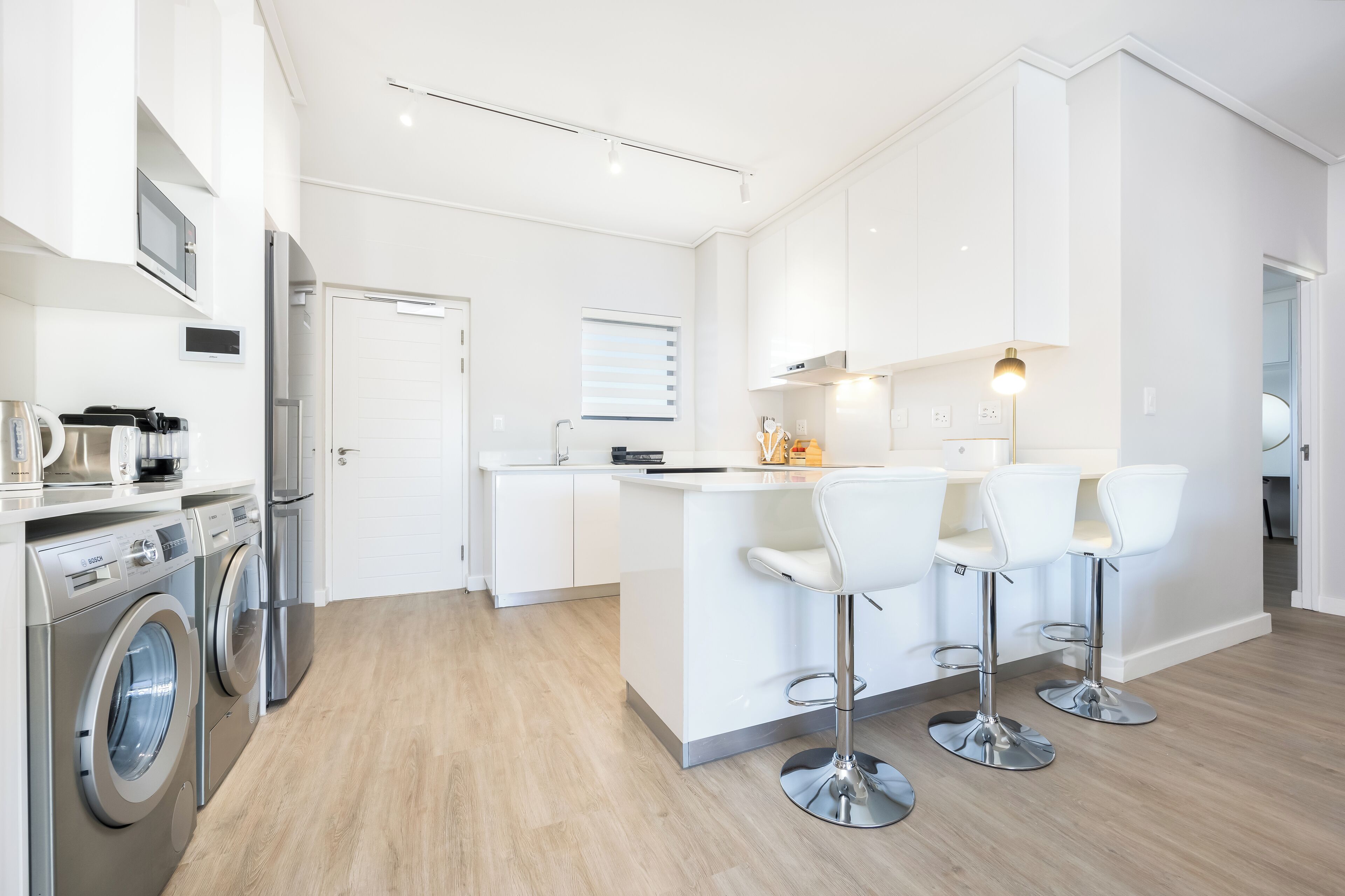 Una cocina moderna con electrodomésticos de acero inoxidable, una isla central con taburetes de bar y un piso de madera clara.