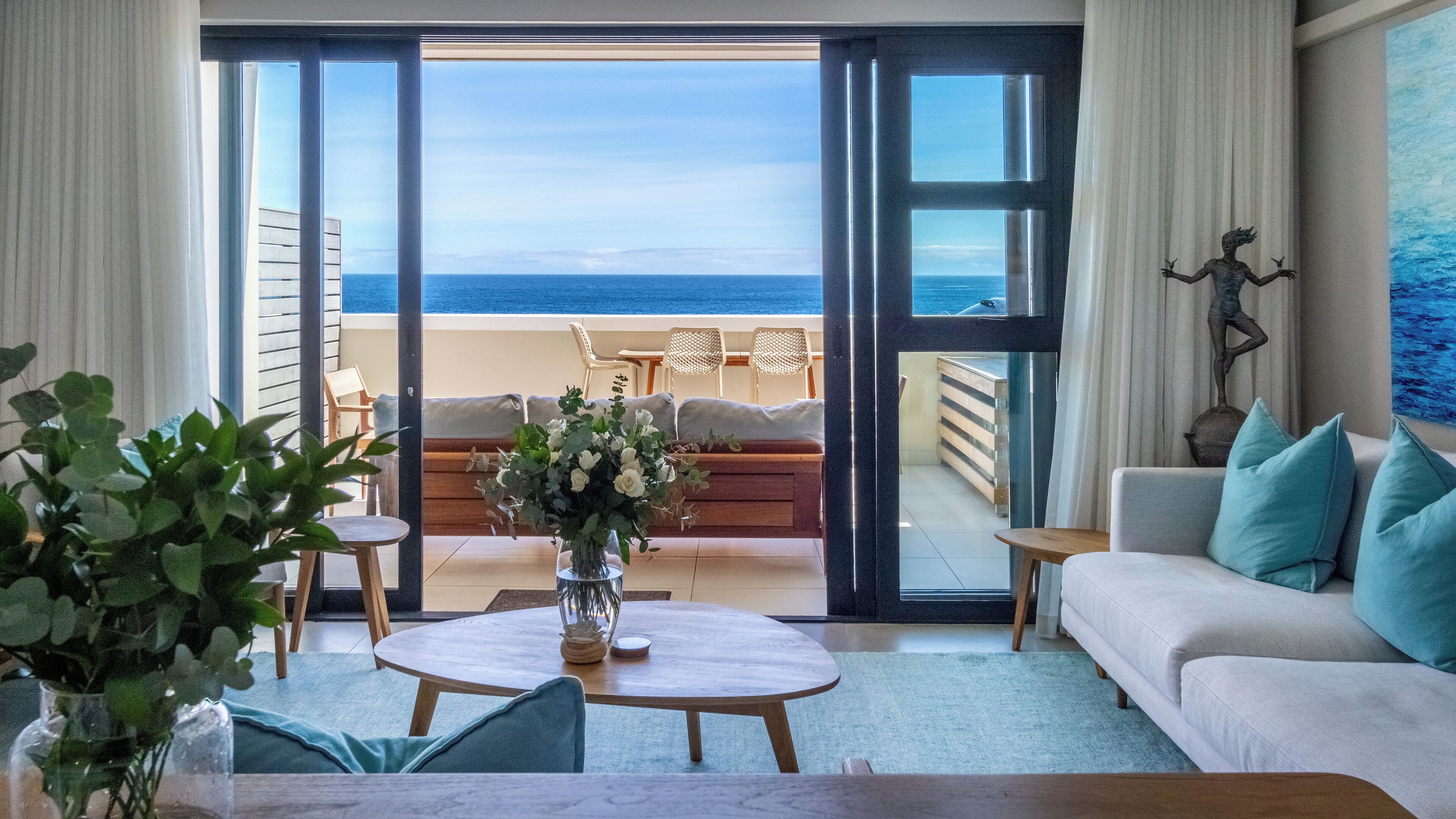 A room with a view of the ocean, a sofa, a coffee table, and a decorative statue.