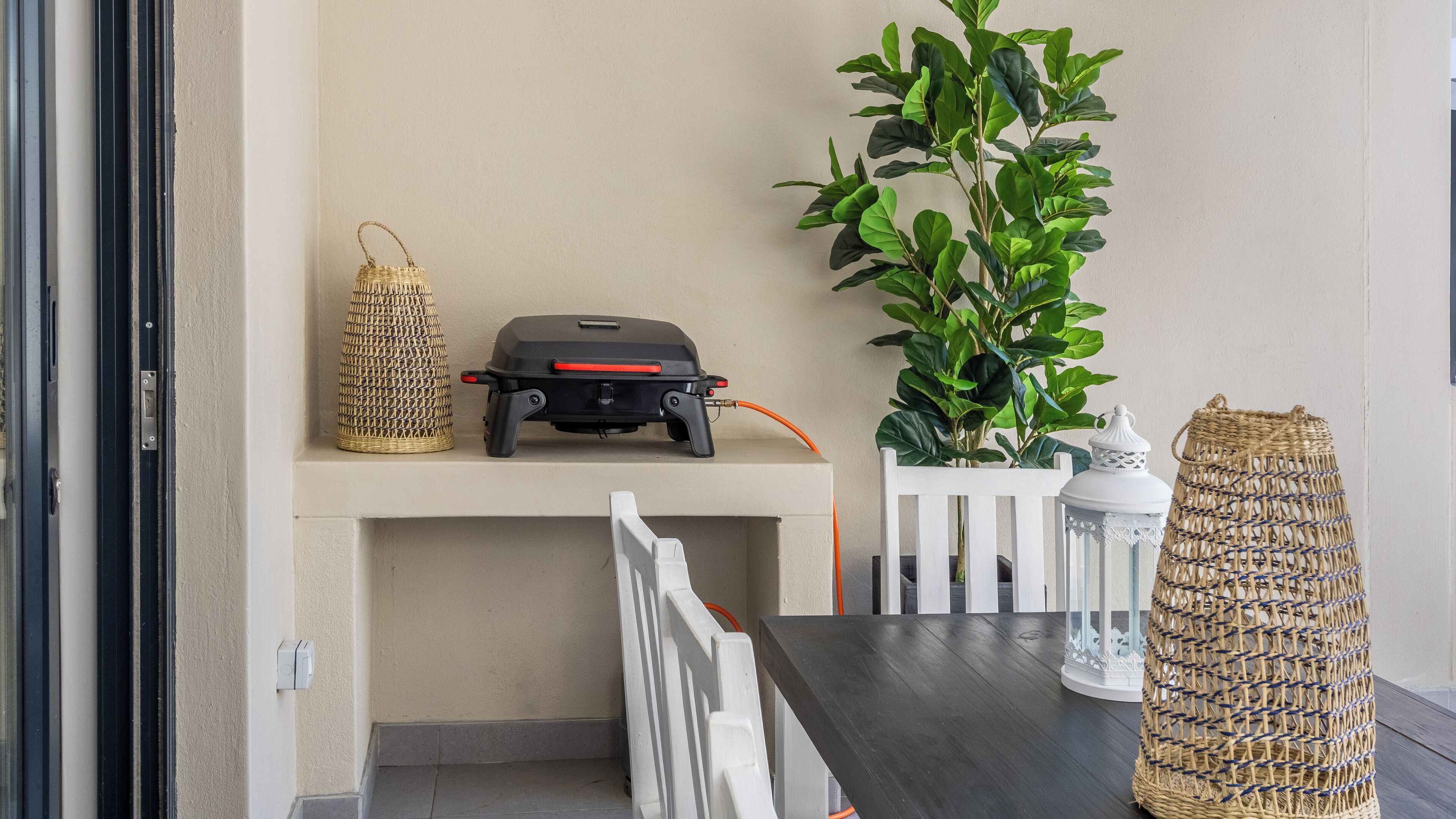 Un espace patio aménagé avec un barbecue, des paniers en osier, une plante en pot et une lanterne.
