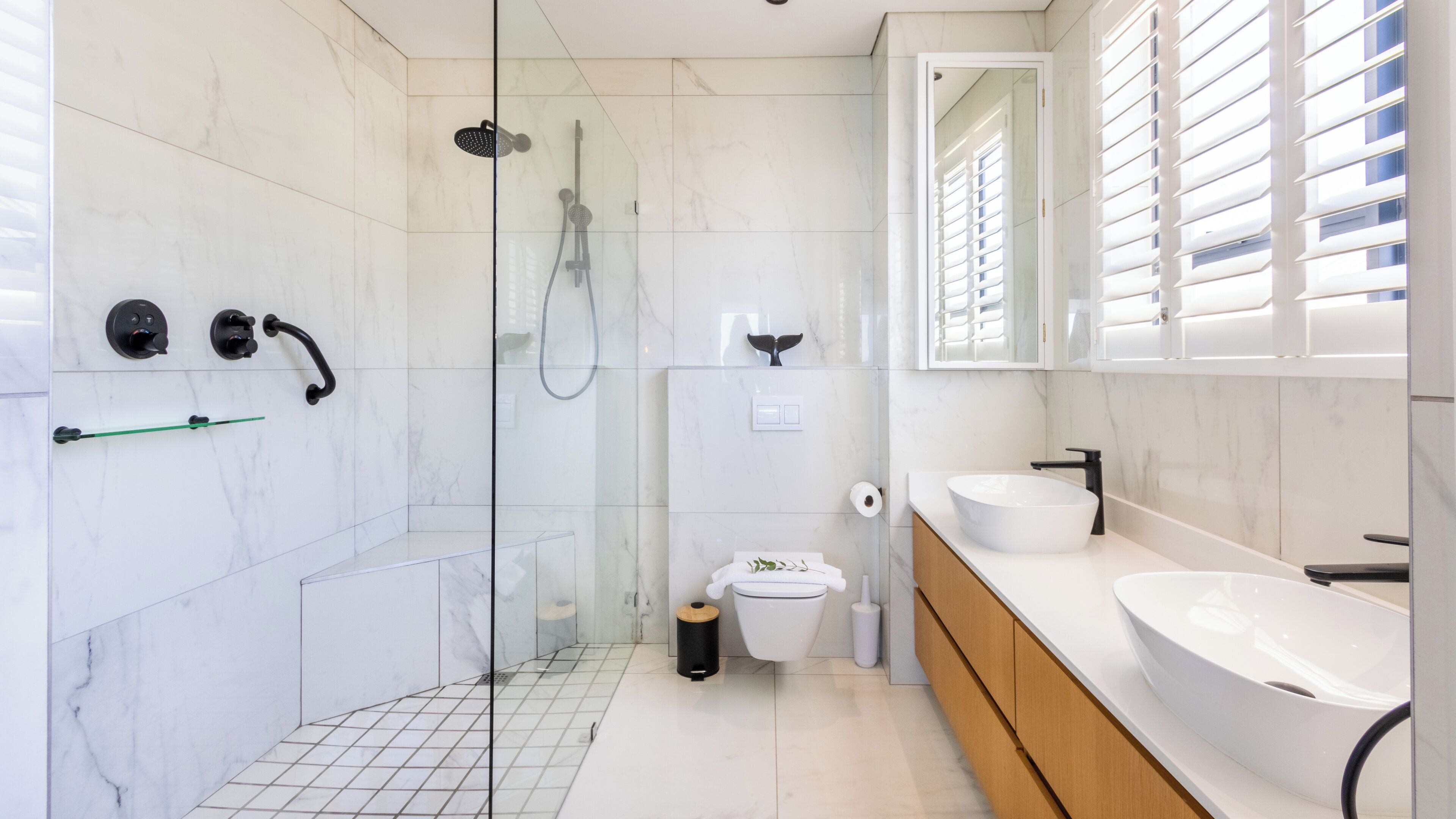 A modern bathroom with a glass-enclosed shower, a toilet, and two sinks.