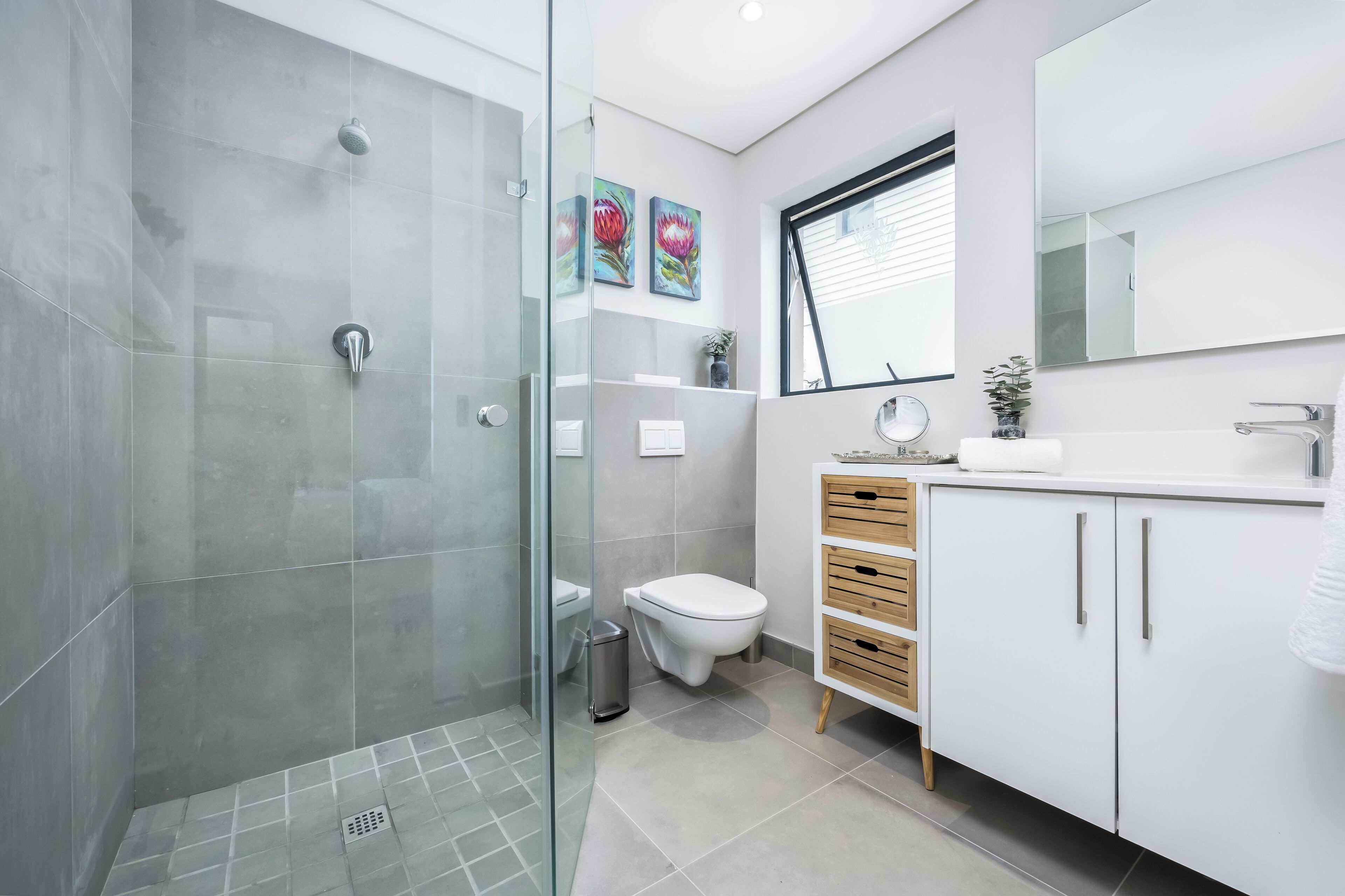 A modern bathroom with a glass shower enclosure, a toilet, and a sink with a mirror above.