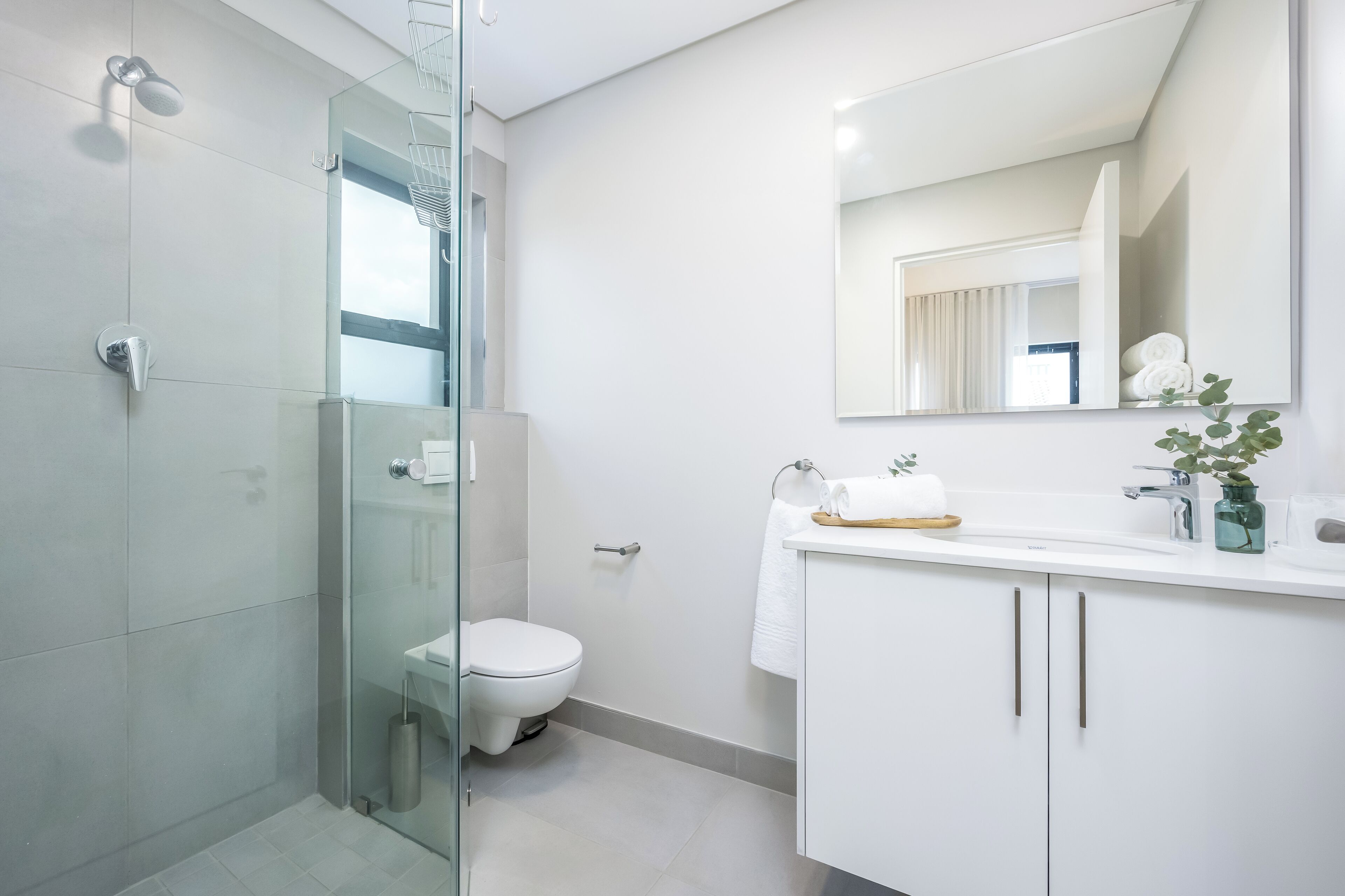 A modern bathroom with a glass shower enclosure, a white toilet, and a vanity with a mirror and towel rack.