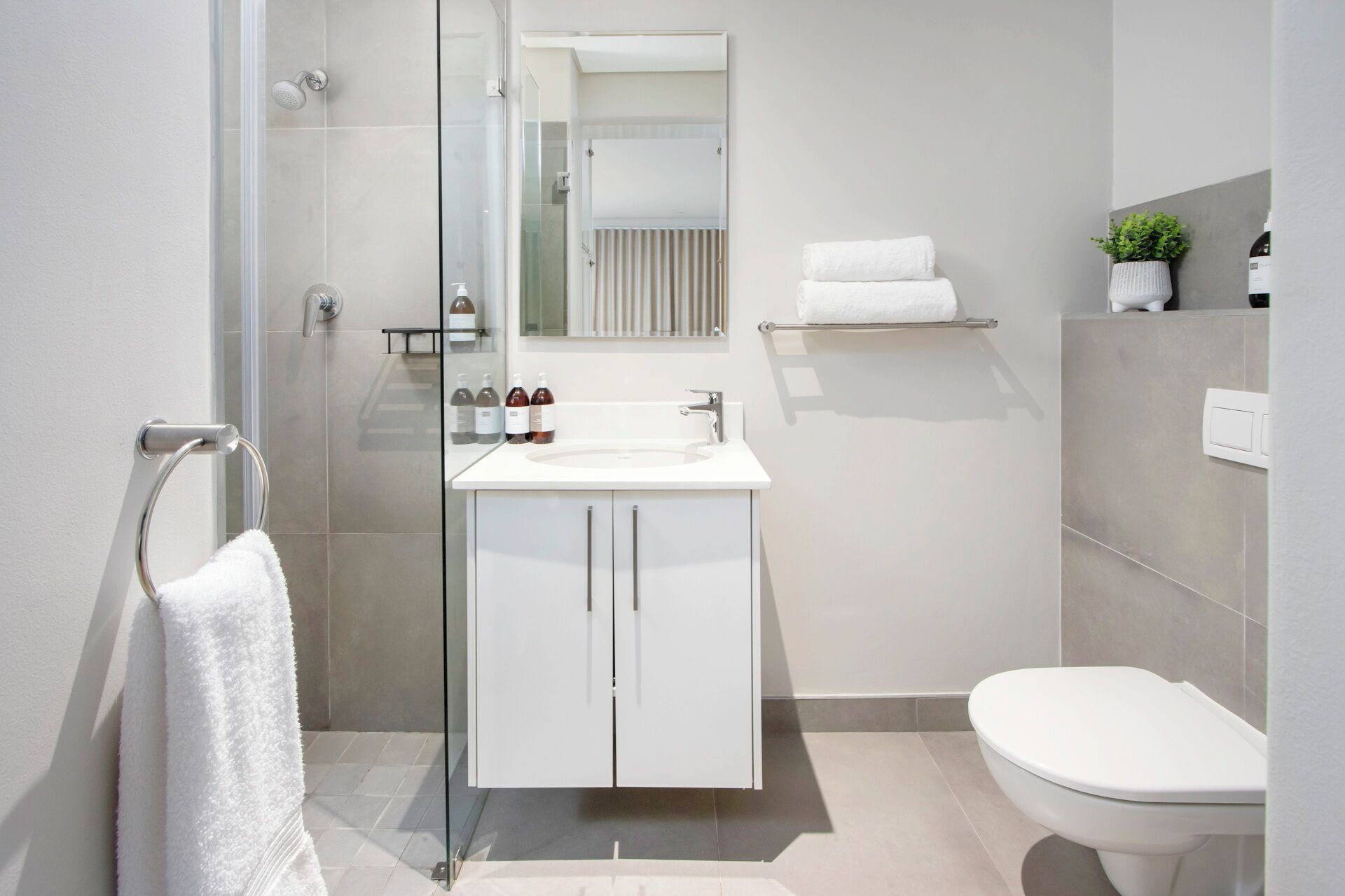 Une salle de bain moderne avec une douche à parois de verre, un lavabo blanc avec un miroir au-dessus et des toilettes.