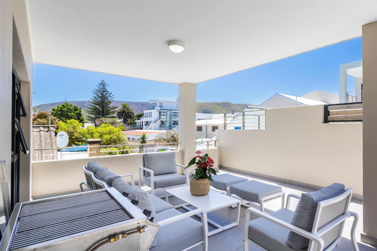Un balcon avec des meubles blancs, une table et une plante en pot.