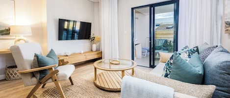 A modern living room with a sofa, armchair, coffee table, and a TV mounted on the wall.