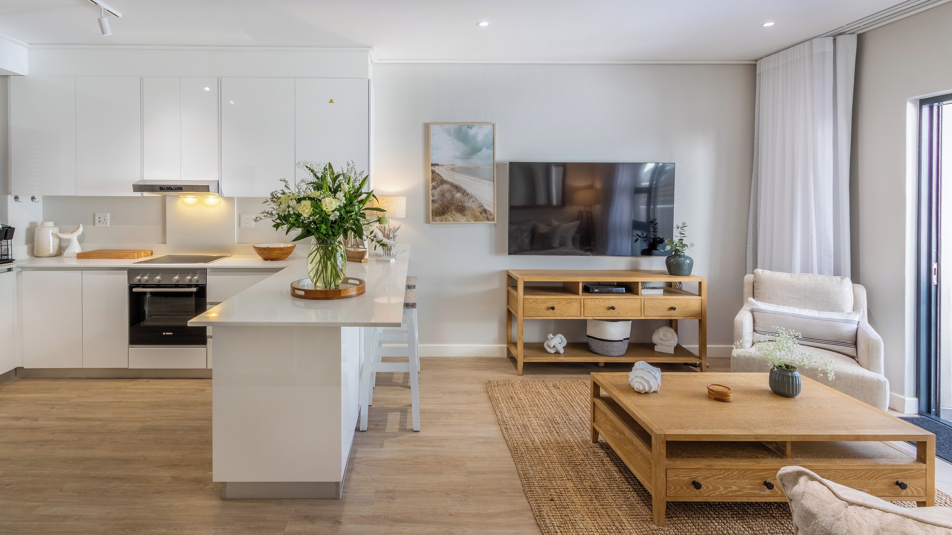 A modern kitchen with white cabinetry, a central island, and a dining area with a wooden table.