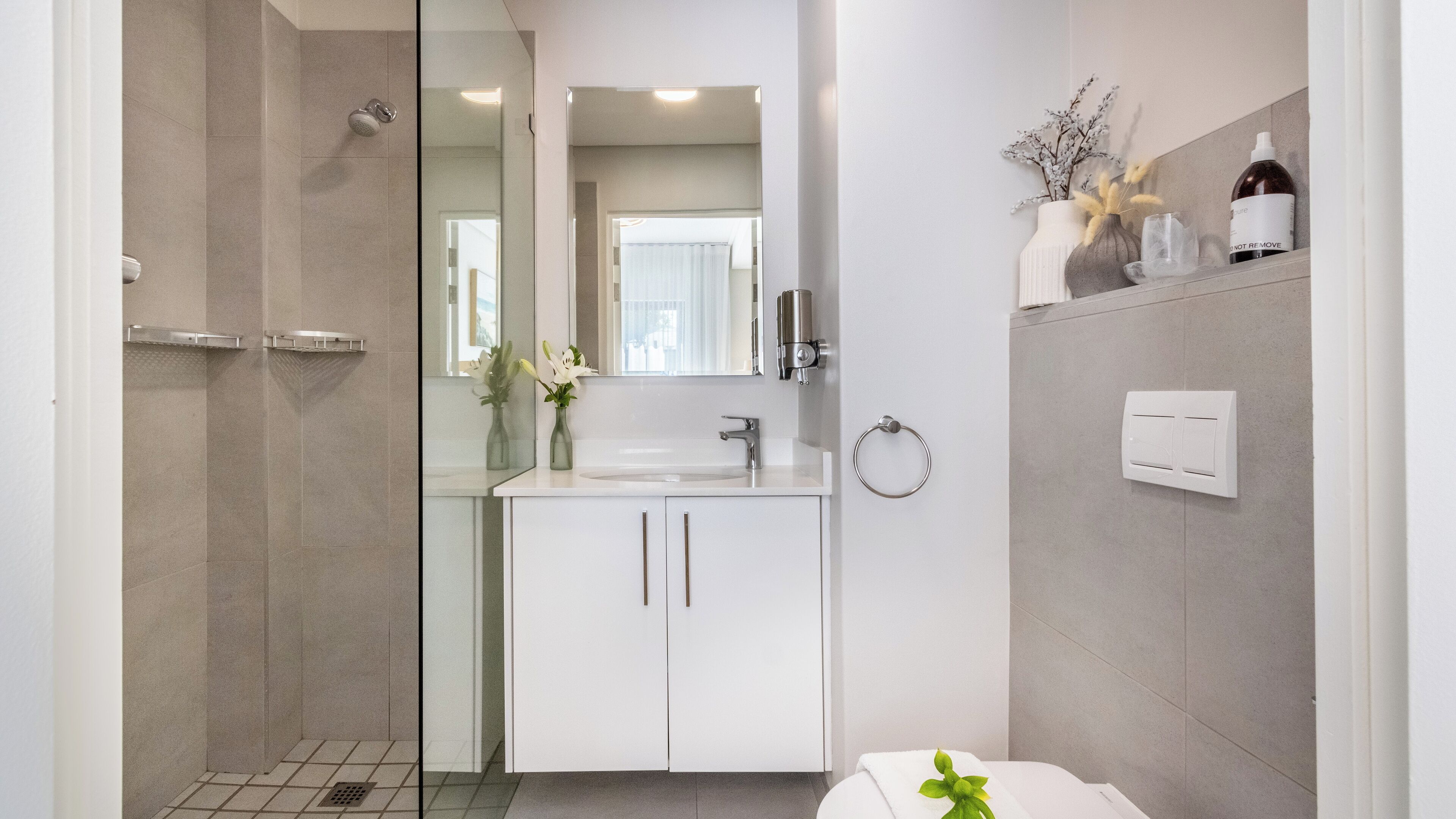Uma casa de banho moderna com cabine de duche em vidro, toucador branco com espelho e porta-toalhas.