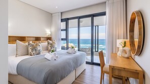 A hotel room with a large bed, a wooden headboard, a view of the ocean, a wooden desk, and a large mirror. - Esplanade Hermanus (Hermanus)