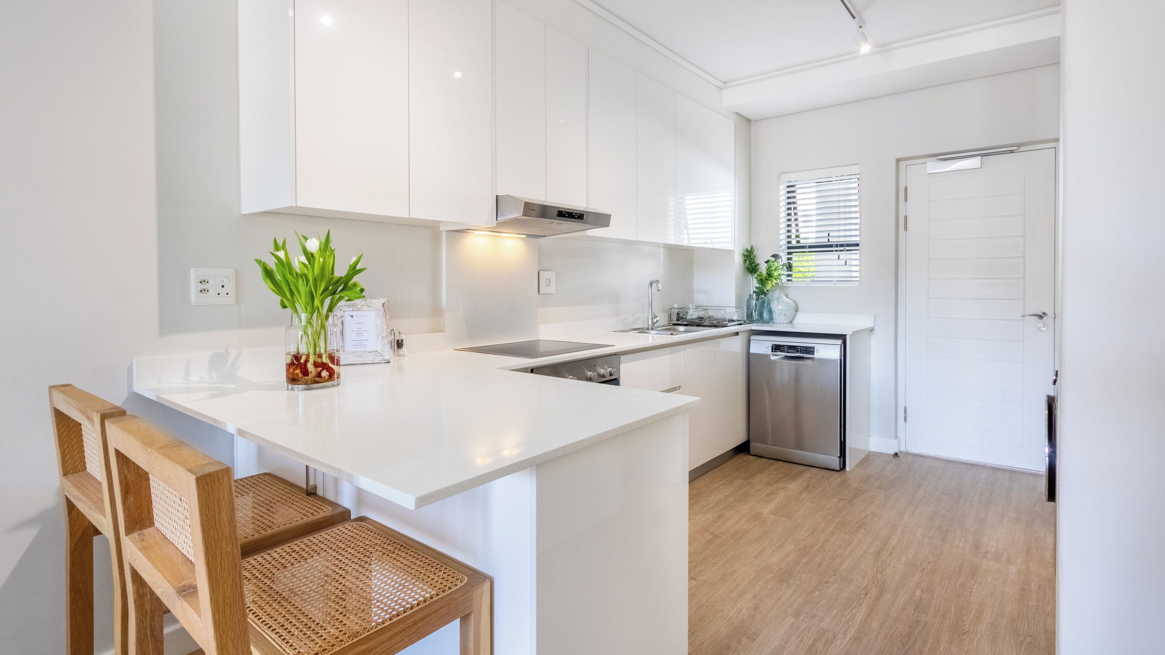 A modern kitchen with white cabinetry, a central island, a built-in dishwasher, and a wooden dining area.