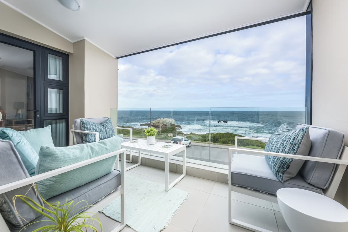 Un balcon avec vue sur l’océan, un canapé, une table et une chaise.