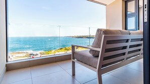 Un balcón con vista al mar, una silla con cojines y una puerta.