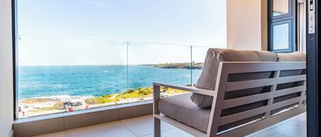 A balcony with a view of the sea, a cushioned chair, and a door.