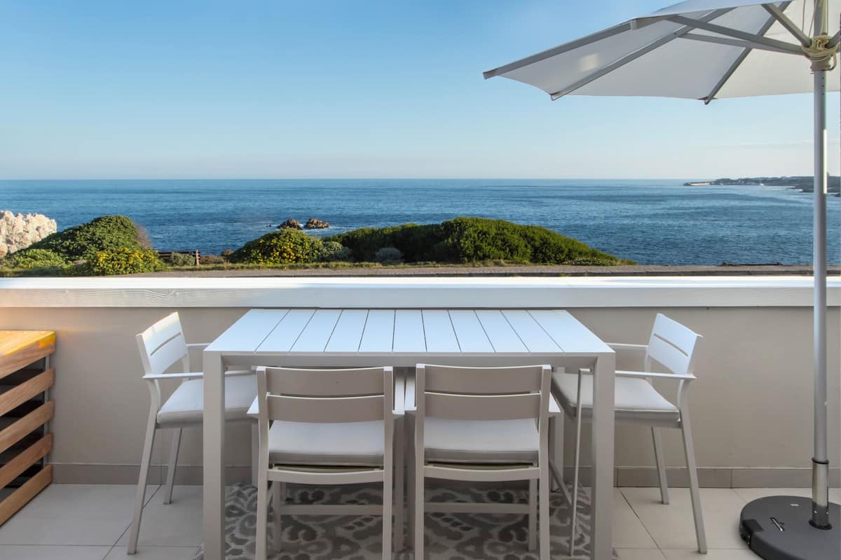 Une terrasse avec une table et des chaises blanches, un tapis à motifs et une vue sur la mer.