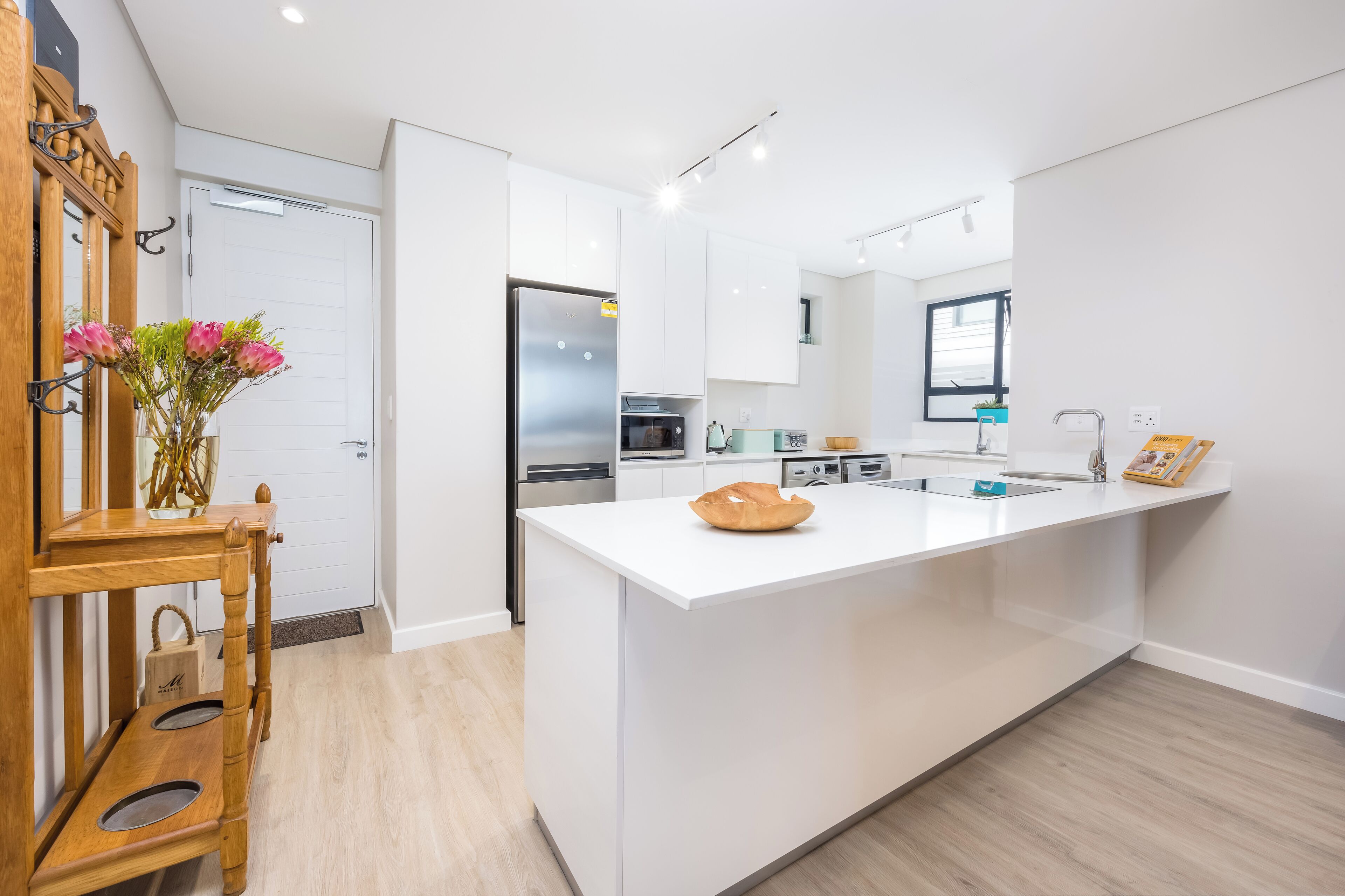 A modern kitchen with white cabinetry, a central island, and a wooden sideboard with a vase of flowers.