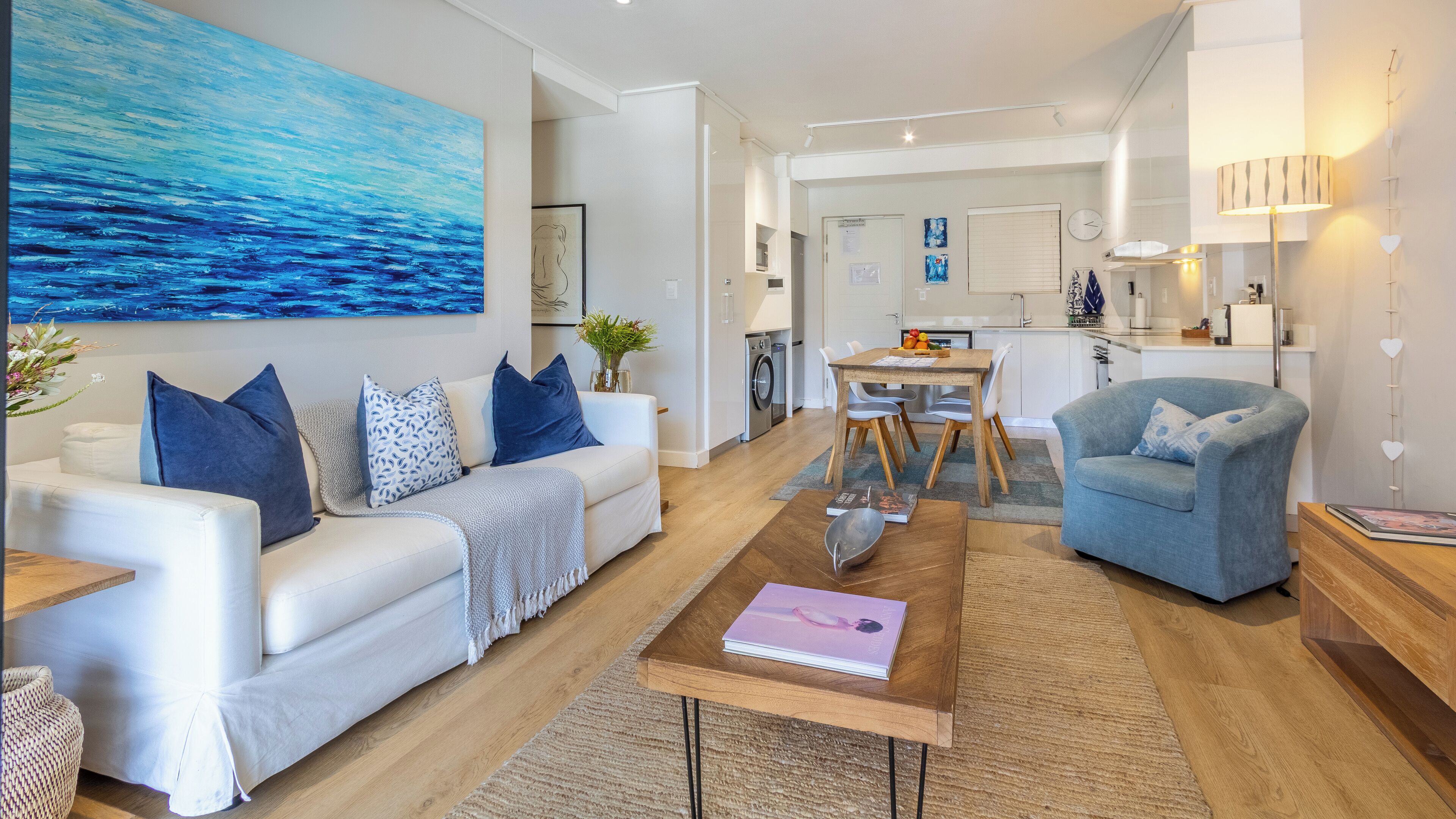 Una sala de estar moderna con un sofá blanco, un sillón azul y una mesa de centro con un libro.