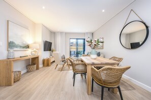 A modern, well-lit room with a wooden dining table, wicker chairs, a large mirror, and a television. - Esplanade Hermanus (Hermanus)