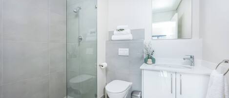 A modern bathroom with a glass shower enclosure, a white toilet, and a vanity with a mirror.