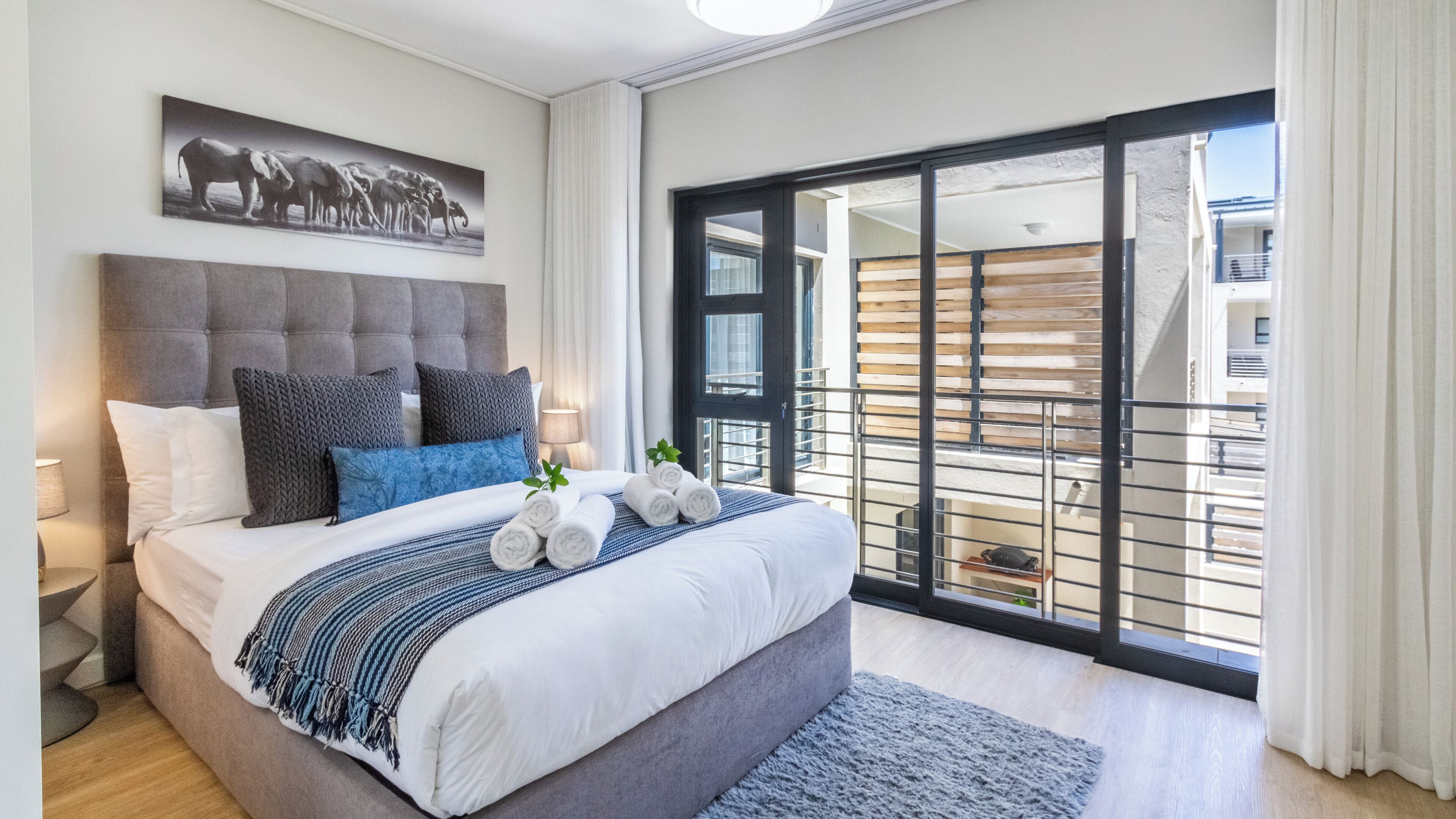 Una habitación de hotel moderna con una cama grande, vistas de la ciudad a trav és de un ventanal corredero y un cuadro enmarcado en la pared.