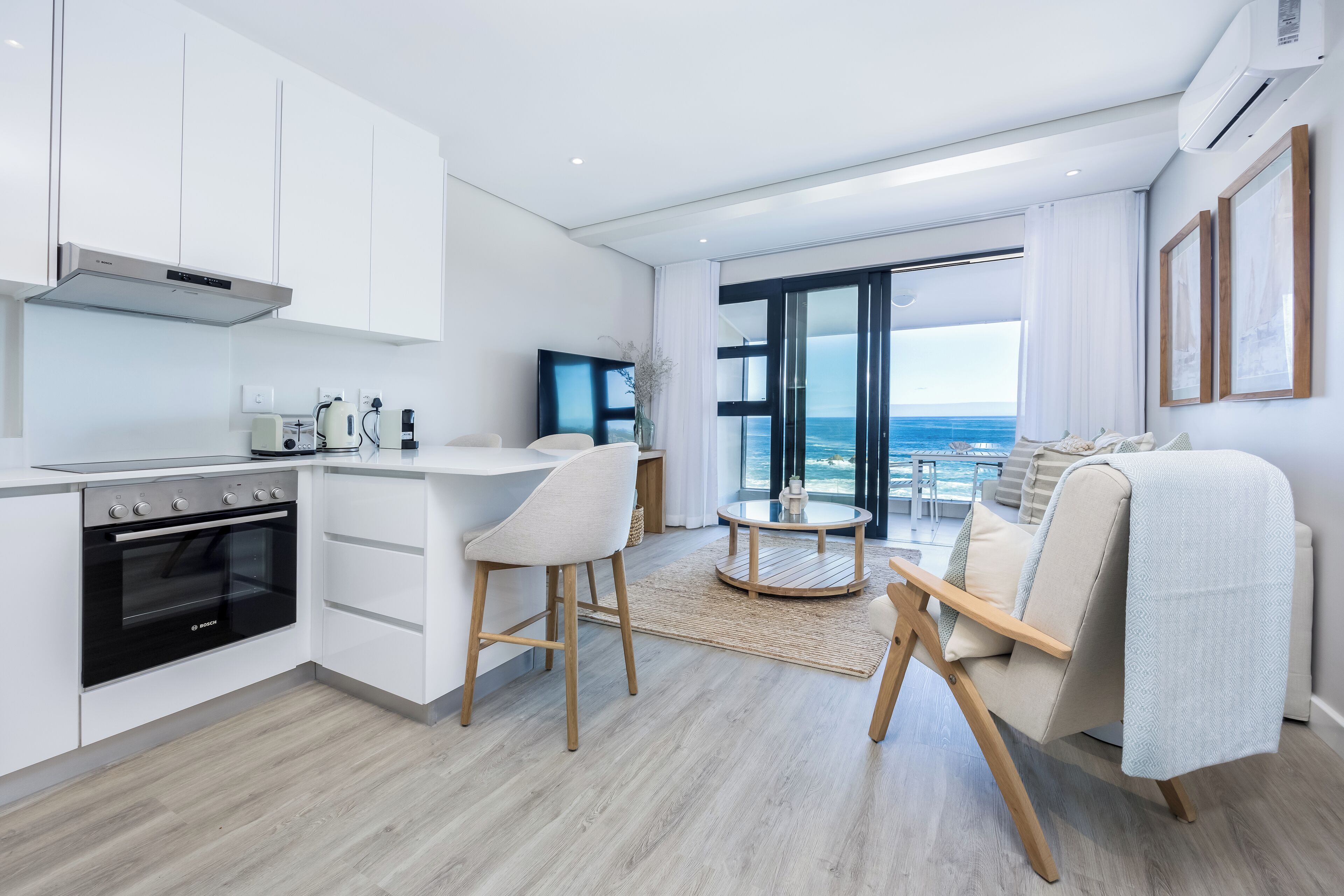 A modern kitchen with white cabinets, a Bosch oven, and a dining area with a round table and two chairs.
