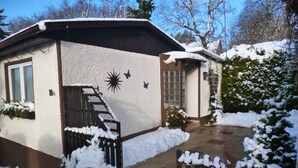 Una casa con exterior nevado, un número '1A' visible en la pared, un pequeño jardín cubierto de nieve y un cielo azul despejado.