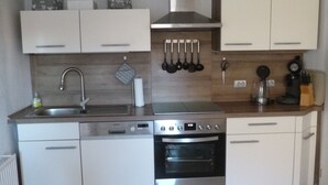 Una cocina compacta con armarios blancos, un lavamanos de acero inoxidable, un horno empotrado y una campana extractora.