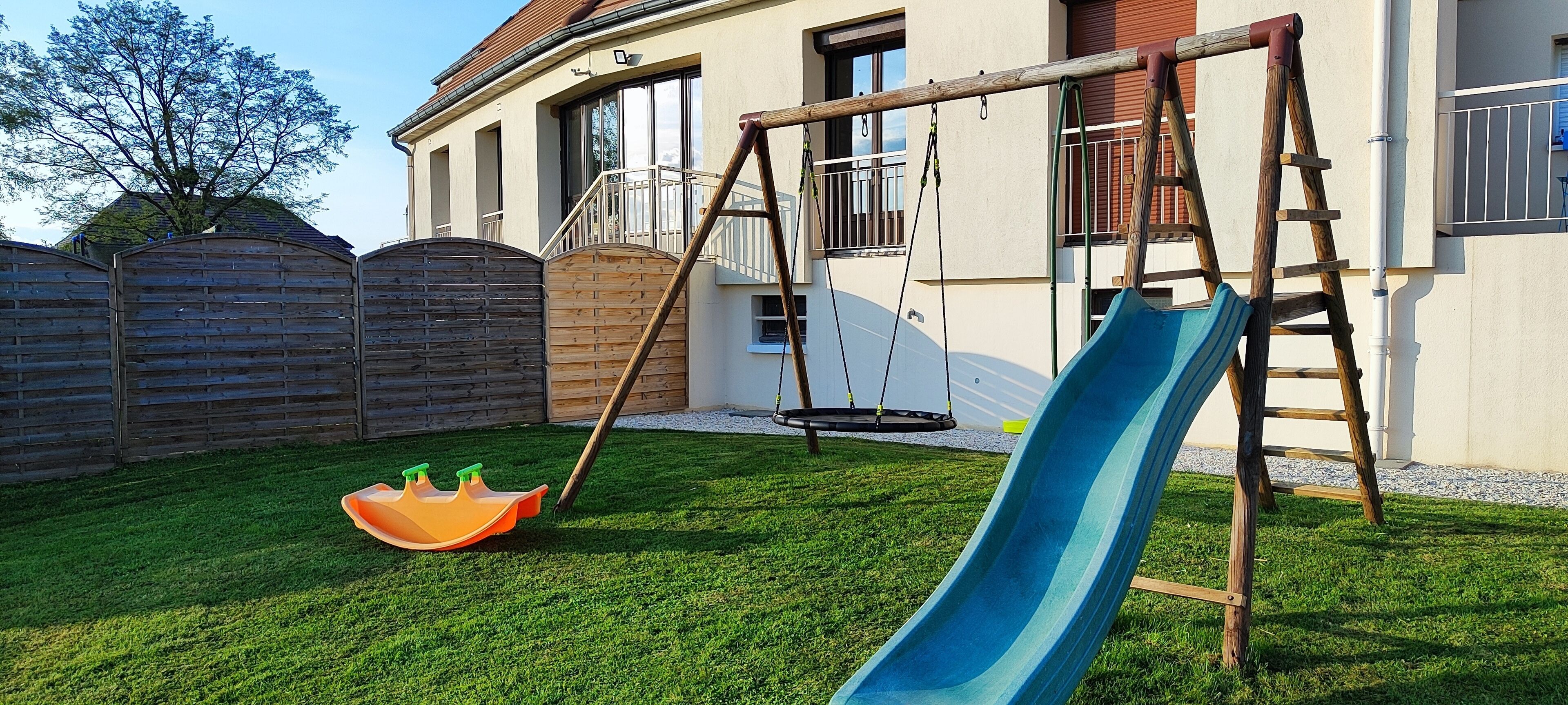 Un jardin avec une balançoire, un toboggan et une clôture en bois.