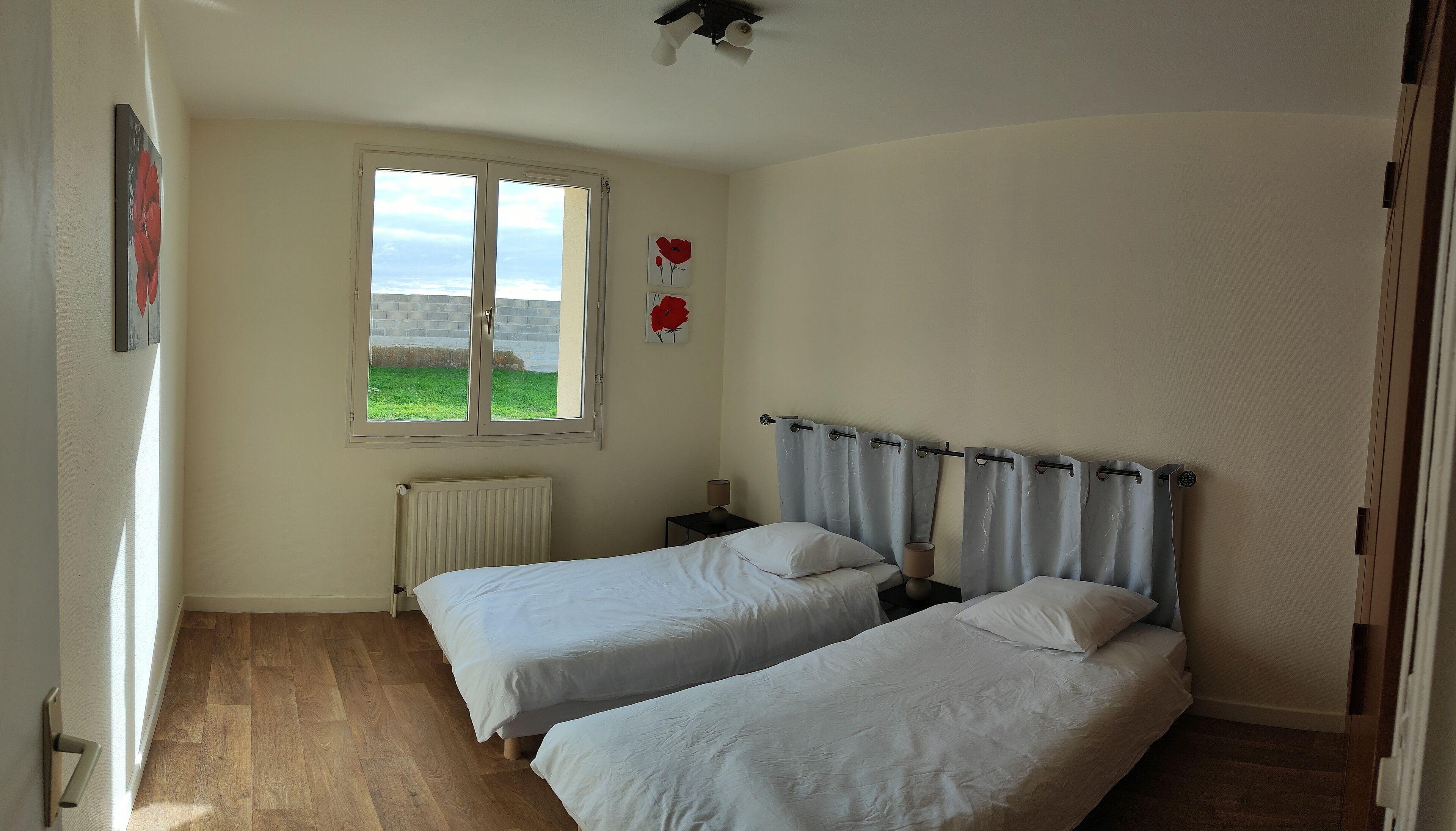 Un dormitorio con dos camas individuales, una ventana con vistas a un campo verde, un radiador y una mesita de noche con una lámpara.