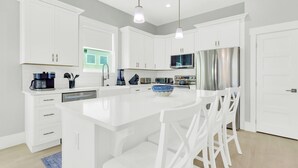 A modern kitchen with white cabinetry, a central island with bar stools, stainless steel appliances, and pendant lighting. - Tailwinds: Free golf cart, Private hot tub, Pool, Game room, 4min to beach (Miramar Beach)