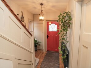A hallway with a red door, a staircase, a chandelier, and a potted plant. - North Bay Cottage (Bridlington)