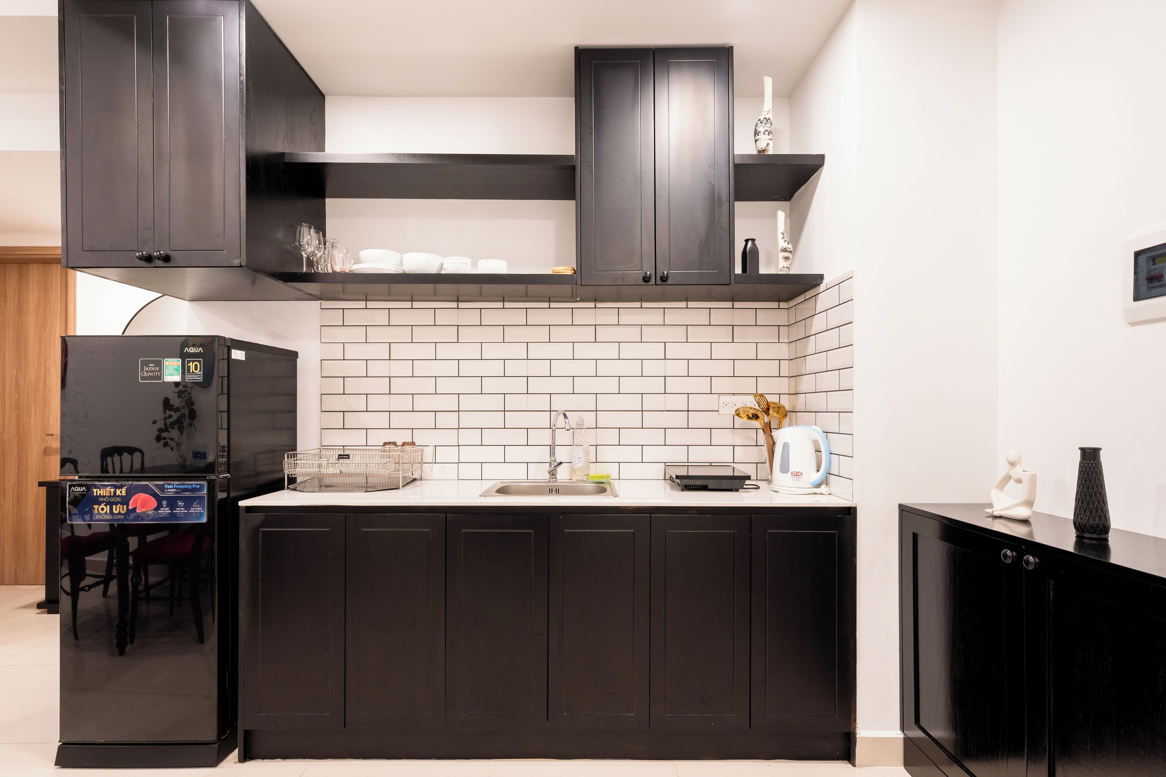 Una cocina moderna con armarios oscuros, salpicadero de azulejos blancos y lavavajillas empotrado.
