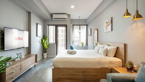 A modern hotel room with a large bed, a TV mounted on the wall, a wooden dresser, and a potted plant.