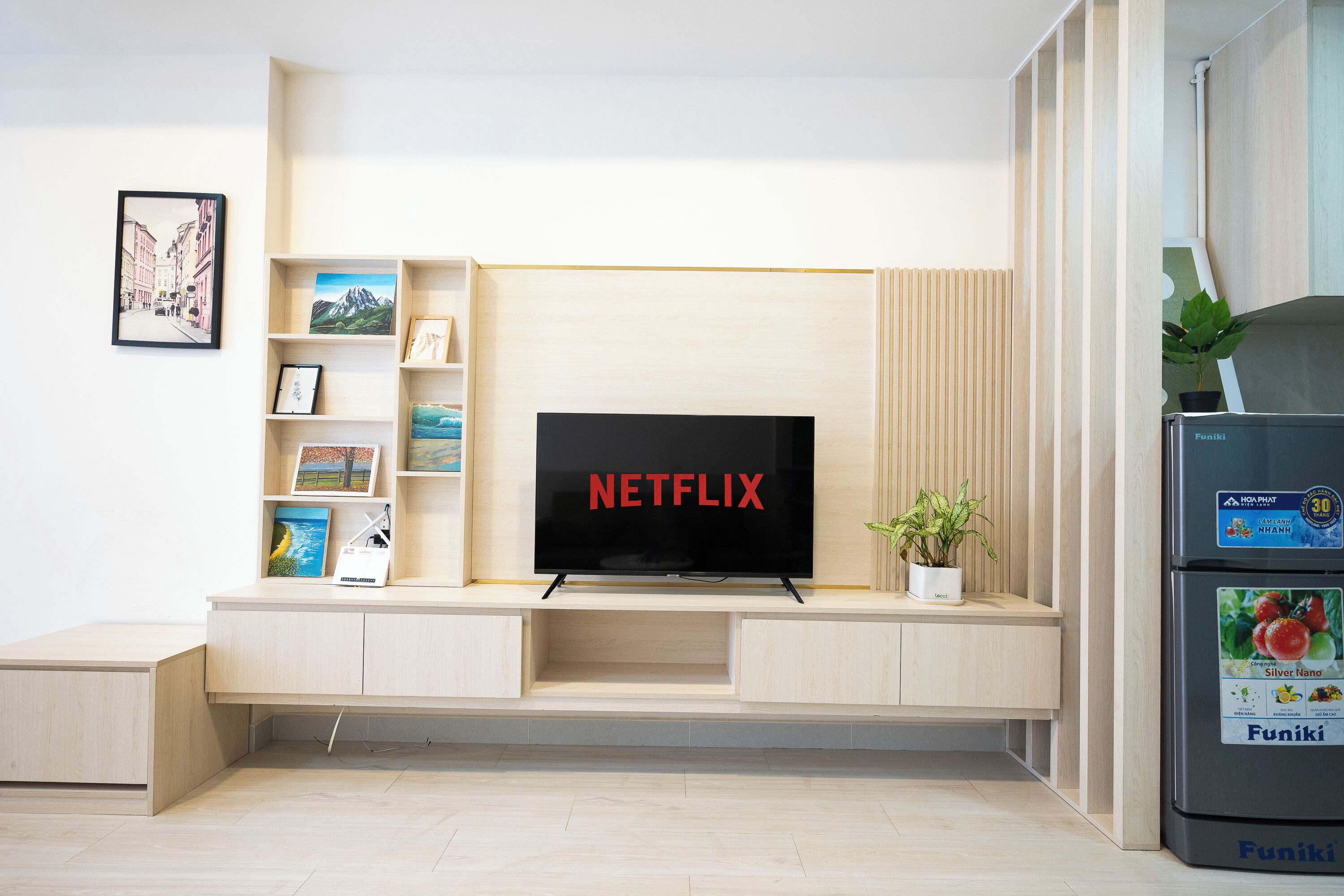 Una sala de estar moderna con una unidad de entretenimiento empotrada, un televisor de pantalla plana que muestra 'NETFLIX', y un refrigerador con la marca 'Funiki'.