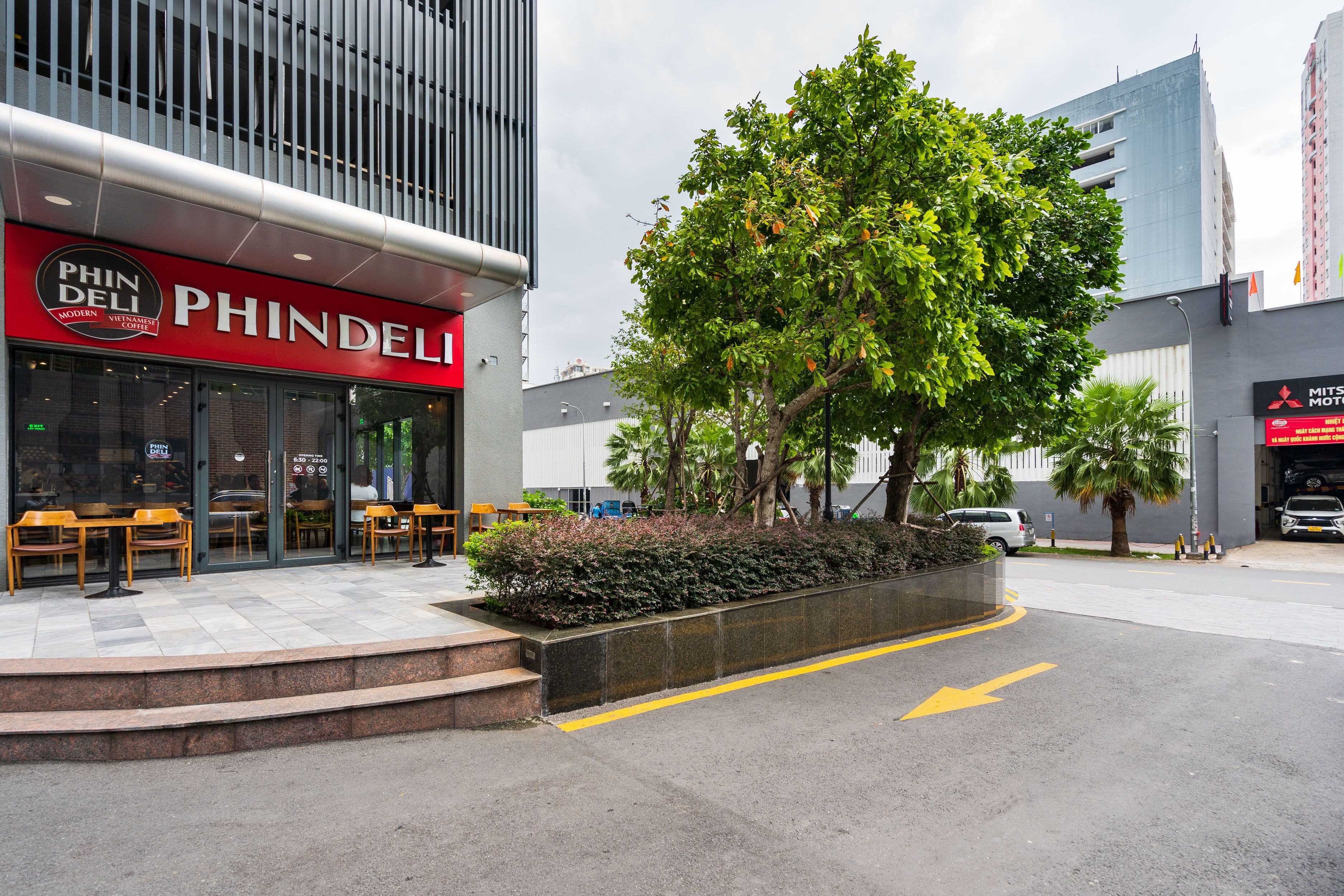 A modern building with a 'PHINDELI' sign, outdoor seating, and a landscaped area with trees.