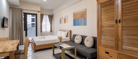 A modern hotel room with a bed, sofa, wooden wardrobe, and a dining area.