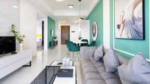 A modern living room with a grey sofa, a white entertainment unit, and a dining area with green chairs.