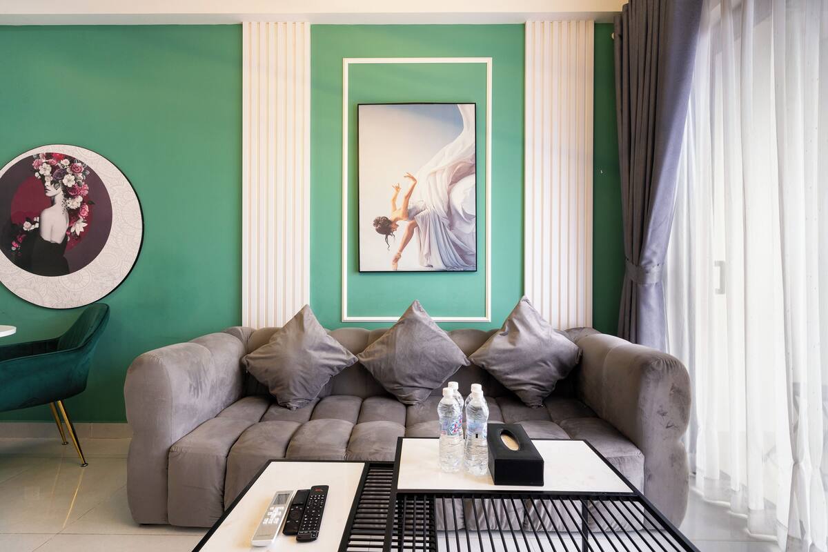 Un salón moderno con un sofá gris, una mesa de centro con controles remotos y una obra enmarcada en la pared.
