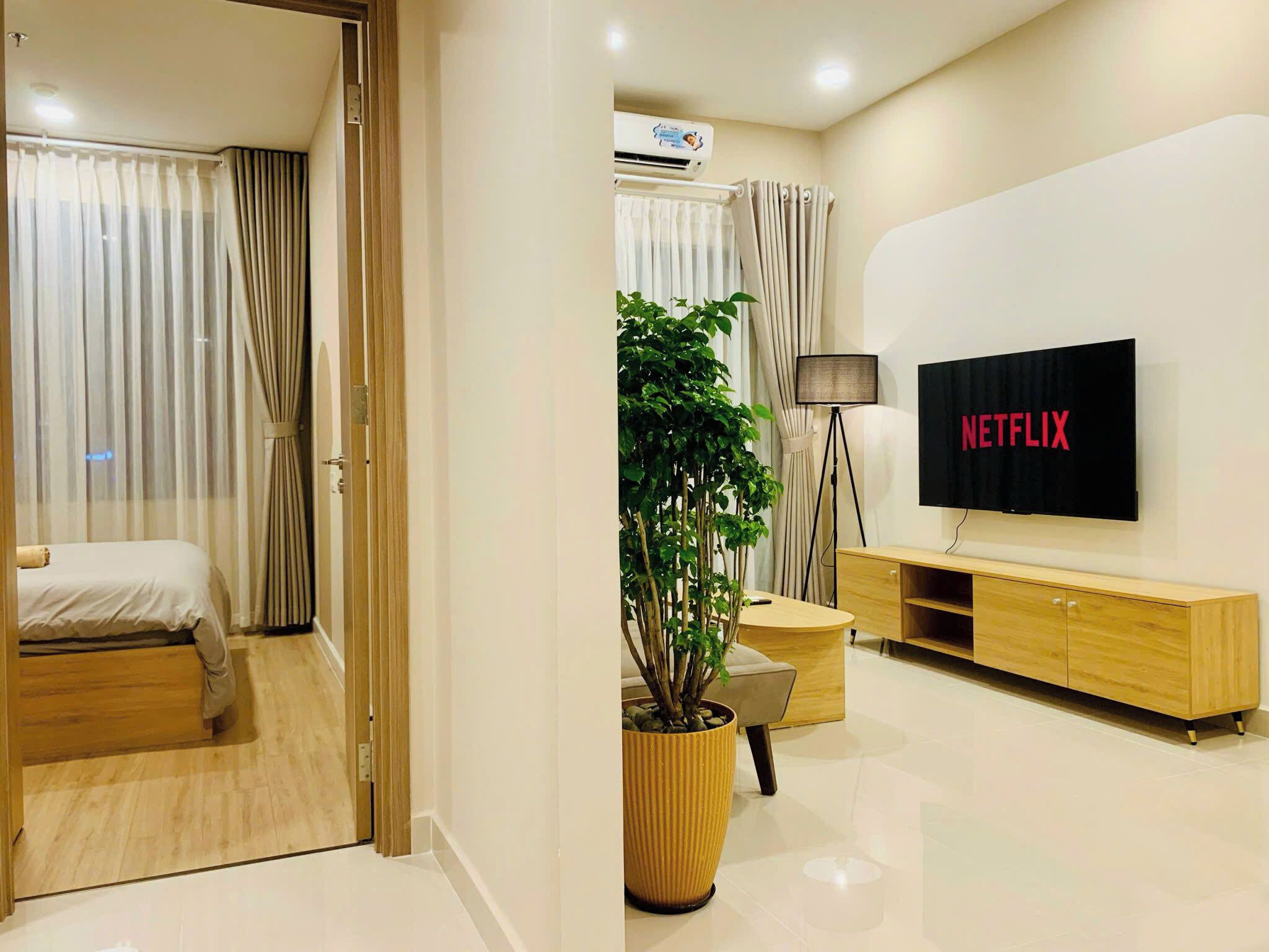 Ein modernes Hotelzimmer mit Bett, Wandfernseher, Topfpflanze und Holzschrank.