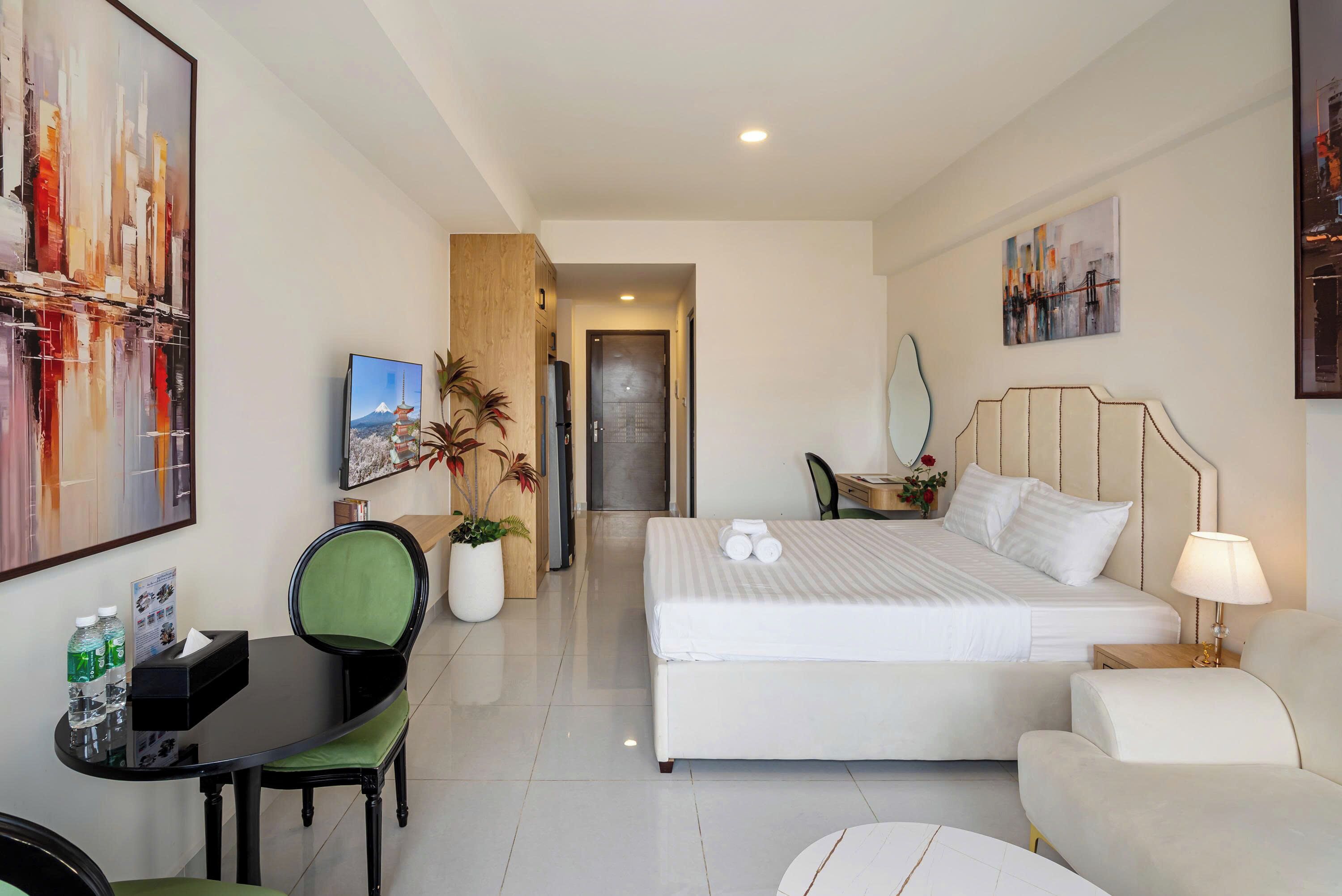 Quarto de hotel com cama, escrivaninha, cadeira, mesa pequena e obras de arte nas paredes.